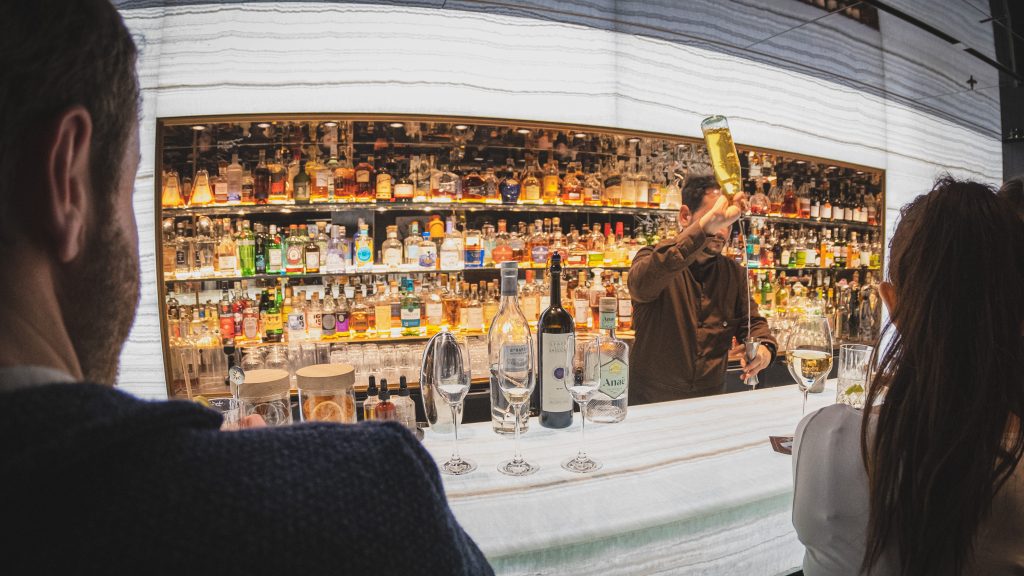 Bartender mixes drinks with bottles in a vibrant Paris bar while customers watch the process.